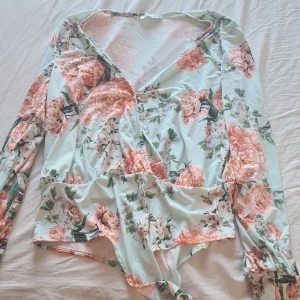 Blommig omlottopp från NLY One - Säljer en vacker blommig omlottopp från NLY One i mjuka pastellfärger. Toppen har långa ärmar och ett romantiskt blommönster i rosa och grönt. Perfekt för en somrig look!