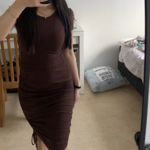 Brun ribbad klänning - Snygg brun ribbad klänning med korta ärmar och en smickrande passform. Klänningen har en knytning i sidan som ger en fin detalj och en slits för extra stil. Perfekt för en chic look!