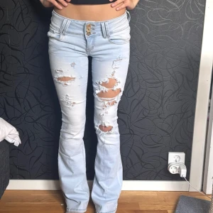 Ljusa slitna jeans - Snygga ljusa jeans med slitningar och bootcut-stil. De har en hög midja och är perfekta för en avslappnad look. Jeansen har en klassisk femficksdesign och stängs med knappar.