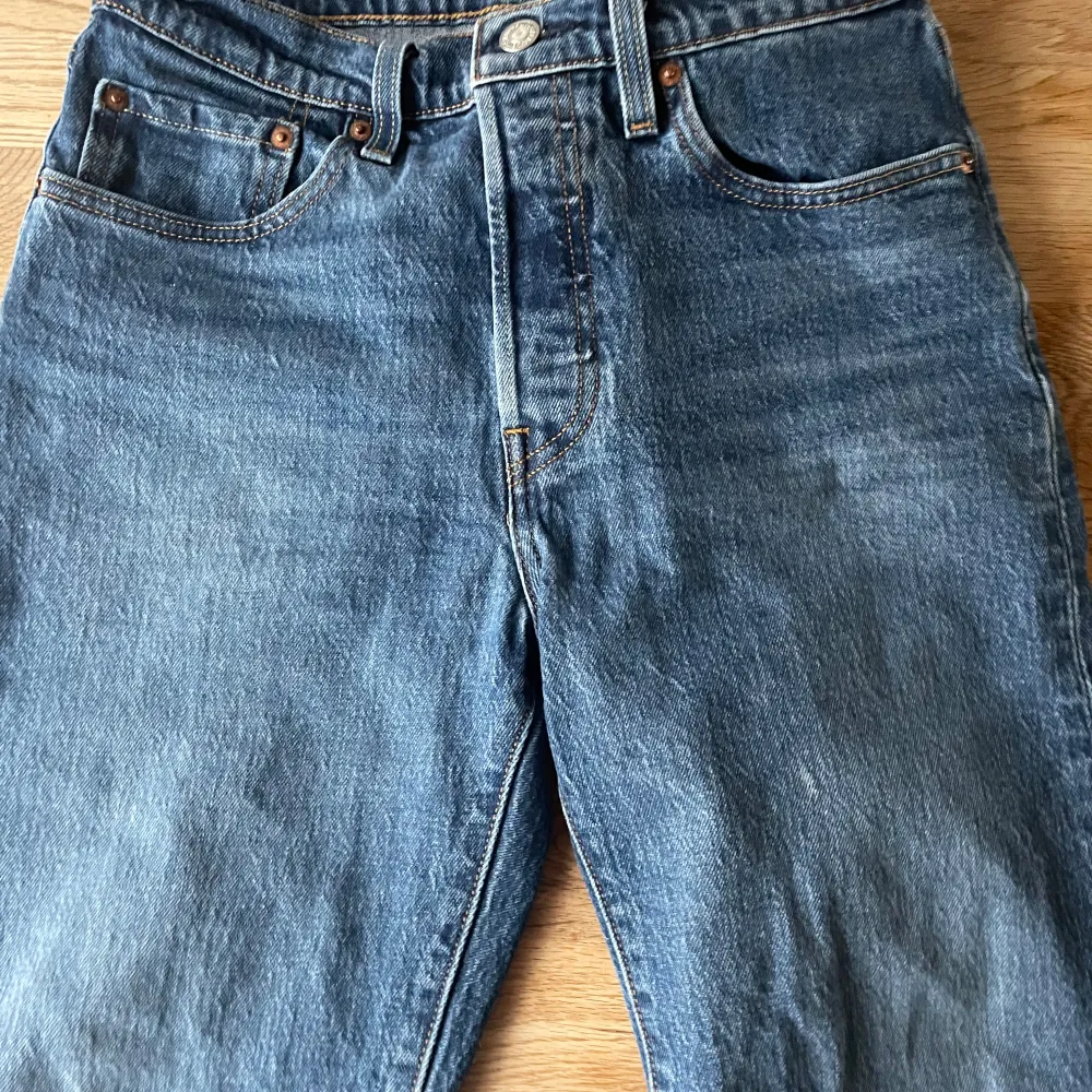 Klassiska blå Levi's 501 jeans med knappgylf. De har en traditionell passform och är perfekta för en avslappnad stil. Märkeslappen syns tydligt på baksidan. Innerbens längden är 62. Farkut & Housut.