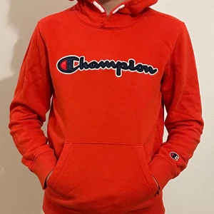 Röd hoodie från Champion - Säljer en snygg röd hoodie från Champion i storlek 150/155 med det klassiska logotyptrycket på bröstet. Tröjan har en stor ficka framtill och en bekväm huva. Perfekt för en avslappnad stil.