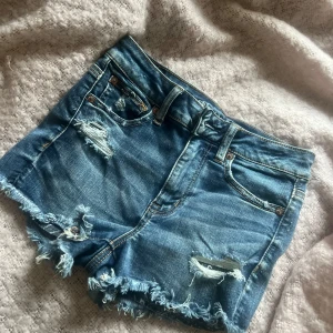 Jeans shorts  - Säljer ett par snygga blå jeansshorts med slitna detaljer,  Högmidjade men går såklart att vika ner som jag har gjort på bilderna, midjemått 33cm. Plagglängd e ungefär 25cm!