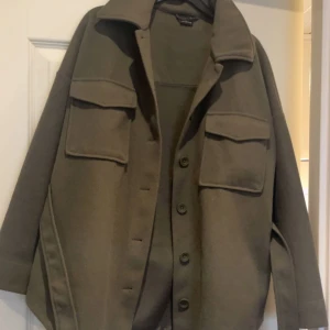 Grön skjortjacka med bälte - Snygg olivgrön overshirt/skjortjacka med knappar och bälte i midjan. Jackan är ”oversize” och passar perfekt nu till våren. Inga defekter!! 