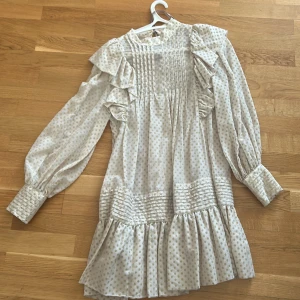 Beige prickig klänning från HM - Säljer en söt beige klänning från HM med prickigt mönster. Klänningen har volanger och långa ärmar med manschetter. Perfekt för en stilfull look! 💫