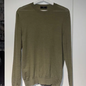 Tröja 100 % merinoull  - Säljer en stilren ogrön tröja från MNG i mjuk merinoull. 100 % merino.Tröjan har en klassisk rund hals och långa ärmar, perfekt för kyligare dagar. Passar både till vardags och mer uppklädda tillfällen.
