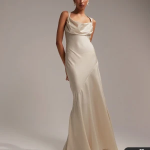 Champagnefärgad långklänning - Elegant champagnefärgad långklänning med smala axelband och öppen rygg. Klänningen har en draperad halslinje och knytning i ryggen för en sofistikerad look. Köpt på asos för drygt 1000kr