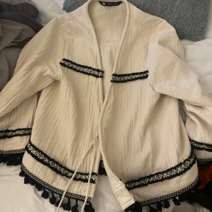 Beige kofta med svarta detaljer - Säljer en beige kofta med svarta detaljer, snören att knyta koftan med. Från zara och använd max 5 gånger. Ordinarie pris 500. Detta pris 300