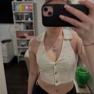 Vit ärmlös knapptopp - Snygg vit ärmlös topp med knappar framtill. Toppen har en krage och är croppad, den har även en halv öppen rygg . Perfekt för varma dagar eller som en del av en lager-på-lager outfit.