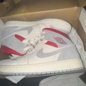 Säljer Air Jordan 1 Mid Heritage –  Nya! - Säljer mina Air Jordan 1 Mid i vit, grå och röd färg. Skorna är i toppskick, endast provade ett fåtal gånger. Perfekta för dig som vill ha en stilren och klassisk sneaker!