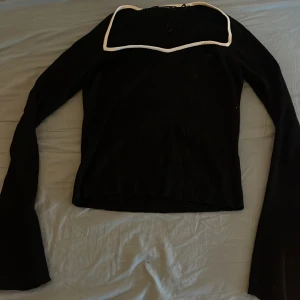 Svart långärmad topp från Gina Tricot - Säljer en stilren svart långärmad topp från Gina Tricot med vita kanter. Toppen har en fyrkantig halsringning och är ribbad för en snygg look. Perfekt för att lyfta din outfit!