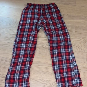 Röd-rutiga byxor från Gina Tricot - Säljer ett par bekväma röd-rutiga byxor från Gina Tricot. Byxorna har en elastisk midja med snörning för extra komfort. Dock ett litet hål vid snöret men det syns ej så mycket.Perfekta för en avslappnad stil.