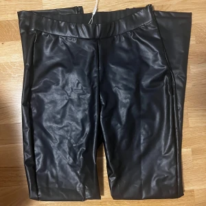 Svarta skinnbyxor - Snygga svarta skinnbyxor med en tight passform från Nelly. Byxorna är ” skinn” inspirerade och har slit längst ned. Finns en dragkedja på väster sida vid höften. Byxorna är endast testade och har alla prislappar kvar. Kom gärna med prisförslag❤️😊