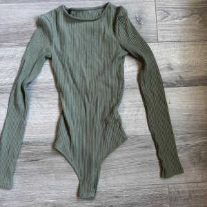 Grön ribbad bodysuit - Snygg grön ribbad bodysuit med öppning i ryggen. Perfekt för att skapa en stilren look. Passar bra till både jeans och kjol. Sitter jättefint på och är i ett stretchigt material