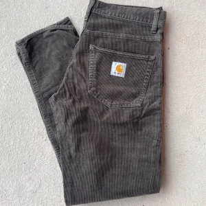Grå manchesterbyxor från Carhartt (slim fit) - Snygga grå manchesterbyxor från Carhartt med klassisk femficksdesign. Byxorna har en diskret randig textur och en logotyp på bakfickan. Perfekta för en stilren  look.