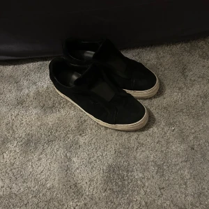 Svarta sneakers från Axel Arigato - Snygga svarta sneakers från Axel Arigato med en stilren design. Skorna har en vit sula och är tillverkade i skinn, vilket ger en lyxig känsla. Perfekta för en avslappnad men stilfull look.