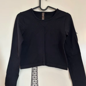 Svart långärmad topp från Only Play - Snygg svart långärmad topp med ribbade detaljer. Perfekt för en stilren look från Only Play i storlek XS. Toppen är croppad och har en rund halsringning. Använd 1 gång. 