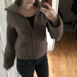 Brun teddyjacka från H&M - Populära bruna teddyjackan med dragkedja framtill. Perfekt för våren och hösten med sin fluffiga och varma design. Knappast använd och är i nytt skick. Jackan har långa ärmar och en hög krage💗
