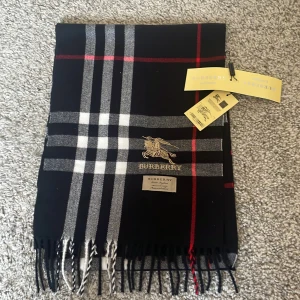 Burberry Halsduk - Säljer en elegant svart rutig halsduk i 100% kashmir. Den har ett klassiskt rutmönster i vitt och rött. Perfekt för att hålla dig varm och stilren under kyliga dagar. Kvaliten är på top och har aldrig kännt på något så mjukt material innan. 