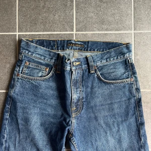 Nudie Jeans  - Säljer ett par klassiska blå jeans från Nudie Jeans Co med raka ben och snygga kontrastsömmar. Jeansen har fem fickor, gylf med dragkedja och Nudie-logga på bakfickan. Perfekta till en avslappnad stil.
