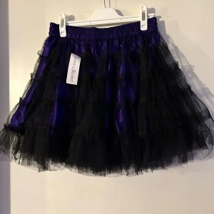 Svart och lila volangkjol onesize - Helt ny kjol i lila och svart. Resår i midjan. Storlek onesize.