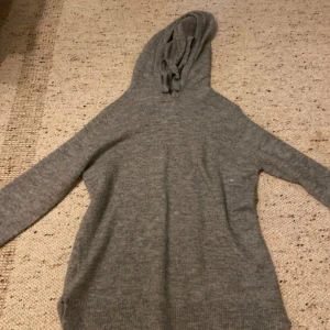 Grå stickad hoodie från Amisu XS - Mysig grå stickad hoodie från Amisu i storlek XS. Tröjan har huva med snörning och långa ärmar. Perfekt för kyliga dagar när du vill vara både bekväm och snygg. Enkel och stilren design som funkar till det mesta.