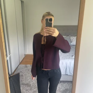 Mörklila omlott cardigan - Säljer en mörklila cardigan med omlott och snörning framtill. Tröjan har långärmade, raka ärmar och en croppad passform. Materialet är mjukt och känns som syntet eller polyester. Perfekt för dig som gillar stilrena detaljer och vill sticka ut med färg.