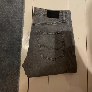 Grå Jack & Jones jeans Tapered/Mike 31/32 - Snygga grå jeans i tvättad look från Tapered/Mike. Modellen är tapered med smalare ben och klassisk femficksdesign. Jeansen har svart patch bak i midjan och är tillverkade i mjukt denimtyg. Perfekta för dig som gillar en avslappnad men stilren vibe.
