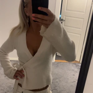 Vit omlottkofta från Gina Tricot - Superfin vit omlottkofta från Gina Tricot i mjuk ullblandning. Koftan har långa ärmar, v-ringning och knyt i sidan. 