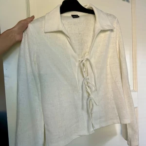 Vit blus med snörning från Gina Tricot - Säljer en vit blus från Gina Tricot i storlek XS. Blusen har lång ärm, krage och snygg snörning framtill som ger en cool touch. Materialet är lätt och har en lite strukturerad yta. Perfekt för dig som gillar stilrena och trendiga plagg. Använd typ 1 gång 🫶🏼
