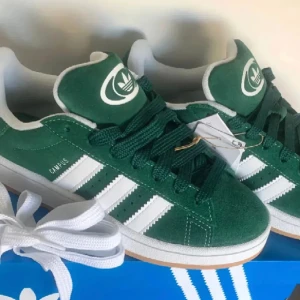 Adidas Campus gröna sneakers mocka - NYA I 38 🌸Gröna Adidas Campus sneakers i mocka med klassiska vita ränder och vit sula. Skorna har rund tå, platt gummisula och snörning. Ikonisk Adidas-logga på tungan och extra vita skosnören medföljer. Perfekta för en streetwear-look.