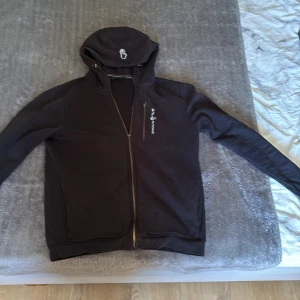 Svart hoodie från Sail Racing med dragkedja - Hej jag säljer min sparsamt använda Sailracing zip Hoodie, den är fint skick men dragkedjans mettal bricka har tyvär lossnat men annars är den i fint skick 