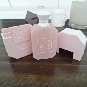 Kayali Yum Boujee Marshmallow EdP - Kayali Yum Boujee Marshmallow är en Eau de Parfum i en matt ljusrosa flaska med vit, diamantformad kork. Doften har noter av fresia, jordgubb, rosa marshmallow, krämig kokos, vispad vanilj och rosa mysk. Flaskan rymmer 100 ml och har en modern, stilren design.