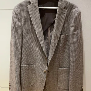 Rutig kavaj från Pour Homme, strl 50 - Snygg rutig kavaj från Pour Homme i beige och bruna toner. Klassisk ofodrad modell med två knappar och två synliga framfickor. Italienskt tyg från Ciatti e Baroncelli.