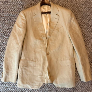 Loro piana linne kavaj - Snygg beige kavaj i linne med klassisk passform och två fickor framtill. Kavajen har ett stilrent snitt, enkelknäppning och ljus innerfoder. Perfekt för dig som vill ha en lätt och luftig kavaj med tidlös look.