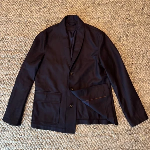 Loro Piana gift of Kings jacka - Exklusiv mörkblå kavaj från Loro Piana, tillverkad i 'The Gift of Kings' ull med Rain System. Klassisk tvåknäppt design, stora fickor fram och elegant insida med kontrastpiping. Perfekt för dig som gillar stilrena och lyxiga plagg.