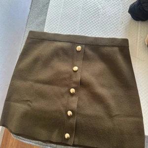 Brun kortkjol med knappar från H&M - Supersnygg brun kortkjol från H&M med raka linjer och dekorativa knappar framtill. Kjolen har en enkel och clean design som är lätt att matcha med olika toppar. Perfekt för dig som gillar stilrena plagg med en twist.