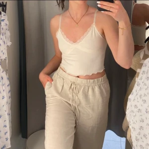 Vit ribbad linnetopp med spets - Supersöt vit/cremefärgad croppad linnetopp med smala axelband och v-ringning. Toppen är ribbad och har fina spetsdetaljer längs urringningen och under bysten. Nederkanten är vågig för en extra gullig touch. Perfekt för varma dagar eller lager på lager.