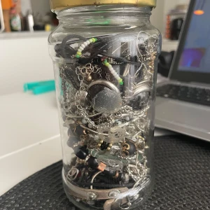 Jewelry jar  - En glasburk fylld med olika smycken som armband, halsband, ringar och örhängen i blandade stilar. 