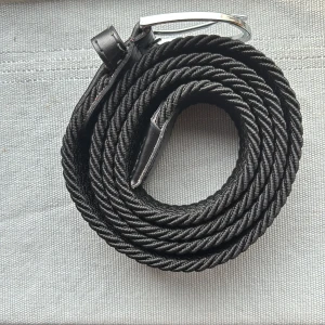 Svart flätat bälte - Snyggt svart bälte med flätad design och detaljer i skinn. Spännet är i silverfärgad metall och ger en stilren touch. Bältet har en rundad form och passar perfekt till jeans eller chinos. Materialet är en mix av syntet och skinn, vilket gör det både flexibelt och bekvämt, har blivit använd en gång.