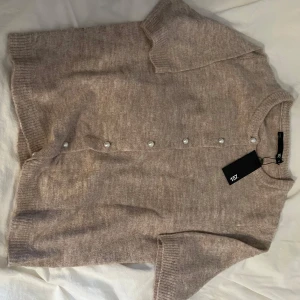 Beige kofta med pärlknappar från 157 - Supermjuk beige kofta från 157 med kort ärm och pärlknappar framtill.  Perfekt och supersnygg att slänga på sig nu när det börjar bli lite kyligt ute. Ny med prislapp kvar.