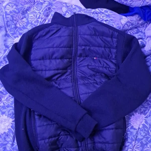 Svart quiltad jacka Tommy Hilfiger M - Snygg svart jacka från Tommy Hilfiger i storlek M. Framsidan är quiltad med dragkedja hela vägen och diskret logga på bröstet. Ärmar och baksida är i mjukt tyg för extra komfort. Perfekt för dig som vill ha en stilren och sportig look.
