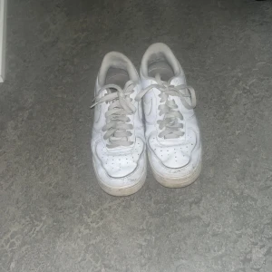 Nike Air Force 1 vita sneakers strl 42 - Klassiska Nike Air Force 1 sneakers i helvitt skinn med perforerad tå, rund tå och snörning. Snygg och tidlös modell med låg profil och diskret Nike-logga på sidan. Perfekta för dig som gillar streetstyle och vill ha en clean look.