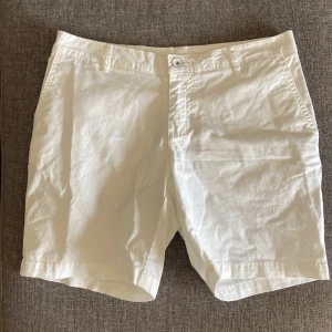 Vita Sail Racing chino shorts - Snygga vita chino shorts från Sail Racing i klassisk modell med fickor fram och bak. Gjorda i mjuk bomull med lite stretch för extra komfort. Perfekta för sommarhäng och chill stil. Passar dig som gillar enkel och clean look.
