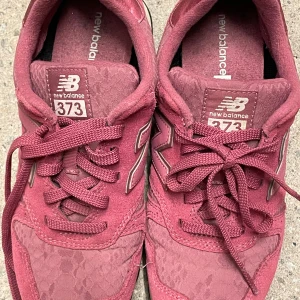 Vinröda New Balance 373 sneakers - Säljer ett par vinröda New Balance 373 sneakers i storlek 39. Skorna har mockadetaljer, klassisk N-logga på sidan och snörning framtill. Yttersulan är svart och mönstrad för bra grepp. Perfekta för dig som gillar sportig och avslappnad stil.