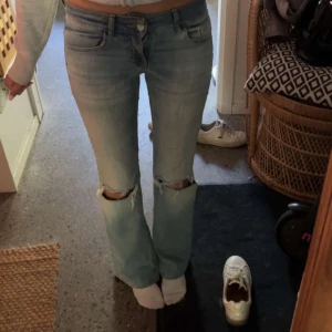 Ljusblå bootcut jeans med slitningar - Säljer ett par ljusblå jeans med bootcut passform och snygga slitningar vid knäna. Jeansen har klassisk femficksdesign, låg midja och är tillverkade i mjukt denimtyg, säljer då dem inte kommer till användning längre💘
