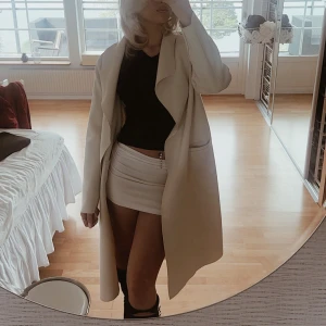 Beige kappa med bälte - Snygg beige kappa med bälte i midjan och stora slag. Jackan har lång ärm och två stora fickor framtill. Perfekt för dig som vill ha en stilren och trendig look under höst och vår. Enkel att matcha med både jeans och sneakers. Storlek L men skulle säga att den passar både M och S