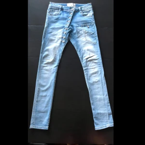 Ljusblå skinny jeans från Chicamour - Säljer ett par ljusblå skinny jeans från Chicamour med cool sned knäppning framtill och klassiska fickor både fram och bak. Jeansen har en tight passform och är tillverkade i stretchigt jeansmaterial. Perfekta för dig som gillar en modern och unik look.