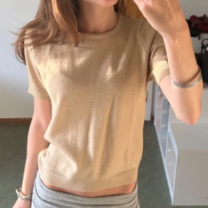 Beige stickad t-shirt - En beige stickad t-shirt i storlek S (skulle säga att den är xs). T-shirten har korta ärmar, rund halsringning och ribbade kanter vid ärmslut och nederkant. Köpt utomlands, vet ej vad butiken heter. Använd en gång 