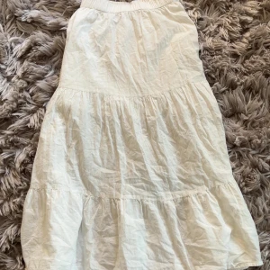 Vit sommarkjol från Lindex - Säljer en vit klänning från Lindex i storlek 146. Klänningen har en luftig och volangig design med resår upptill och flera lager i kjolen. Perfekt för varma dagar och har en enkel, fräsch look. Materialet är mjukt och känns skönt mot huden.