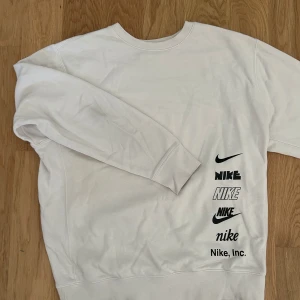 Vit Nike sweatshirt med tryck - Vit sweatshirt från Nike med flera olika svarta Nike-loggor tryckta på framsidan. Tröjan har rund hals, långa ärmar och är tillverkad i mjuk bomullsmix. Skit skön och snygg. Bra passform och mycket bra skick
